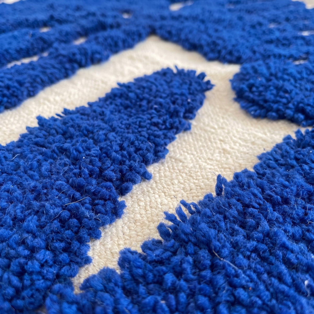 Gros plan sur un motif du tapis berbère Martil, fond écru ras, formes bleu roi en relief