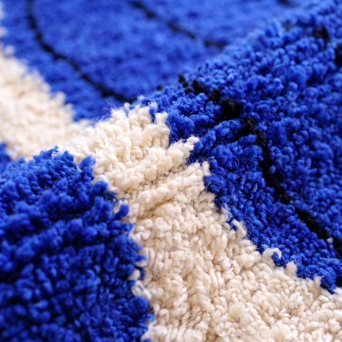 Gros plan sur un motif du tapis berbère Tizgane, fond bleu roi vif à poil long