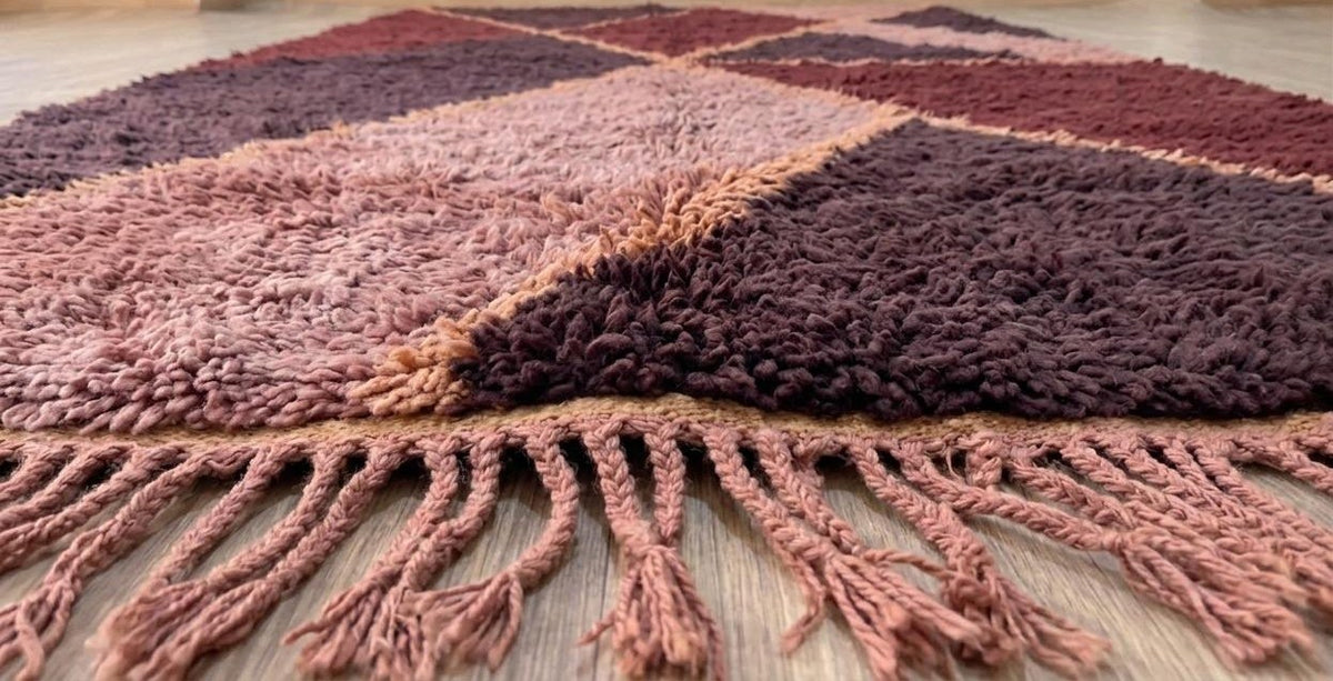 Tapis berbère graphique bordeaux et rose Amzalen posé au sol vu de côté, noué main au Maroc