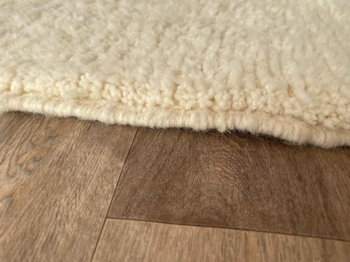 Gros plan sur le coin relevé du tapis berbère Zandir, épaisseur du poil long et dos tissé à la main