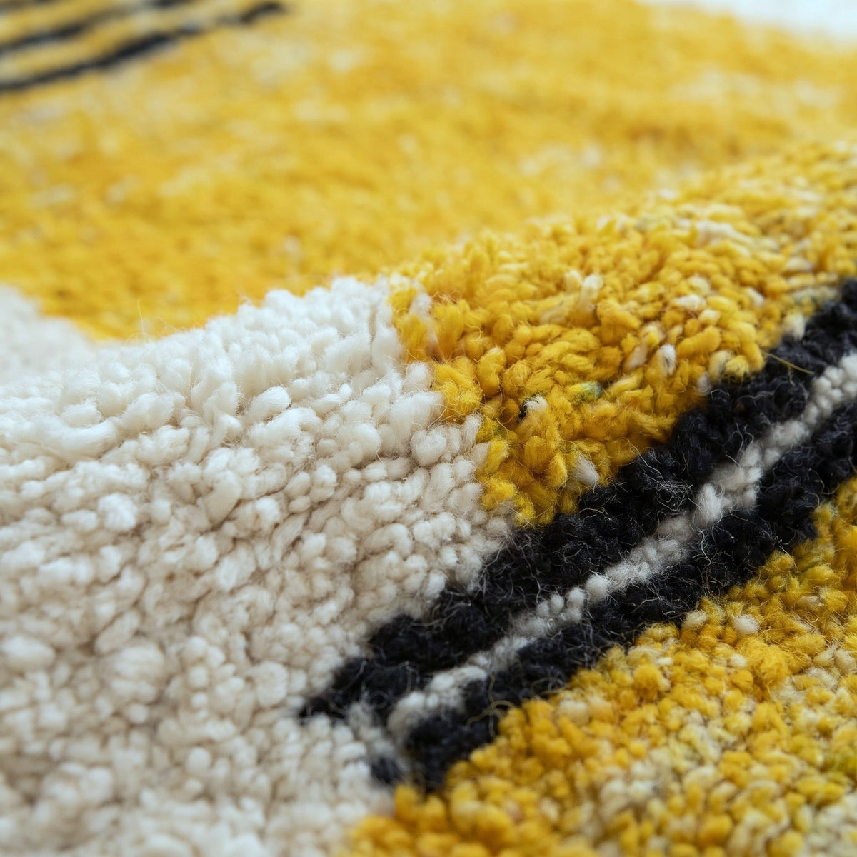 Gros plan sur un motif du tapis berbère Zandir, fond écru à poil long, bandes noires