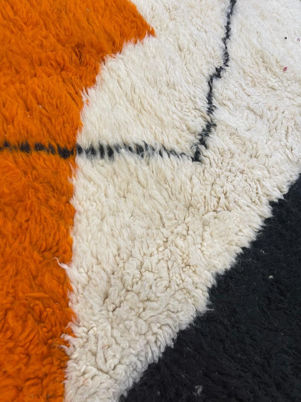 Gros plan sur la laine du tapis berbère Mouzal, laine de mouton au poil long, noire et orange