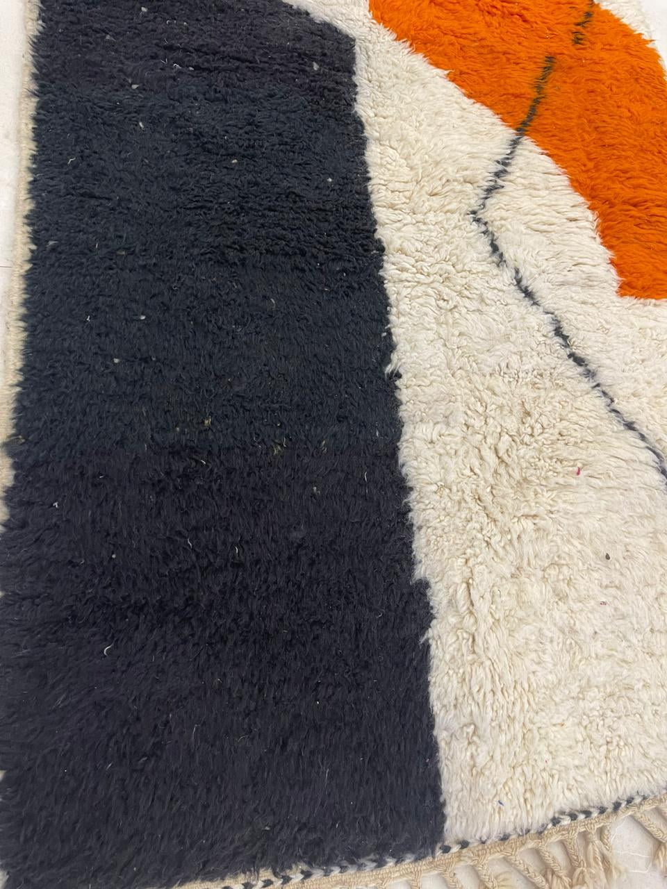 Gros plan sur un détail du tapis berbère Mouzal, poil long et motif noir et orange vus de près