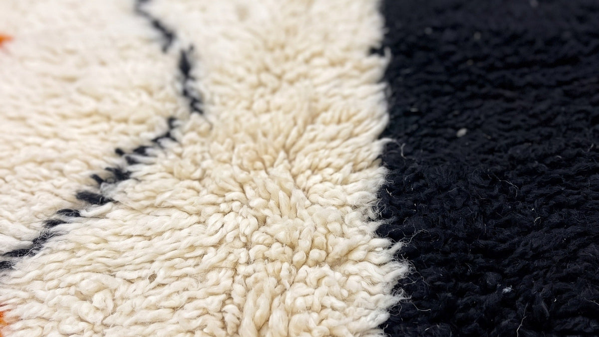 Gros plan sur la laine du tapis berbère Mouzal, poil noir et orange noué à la main