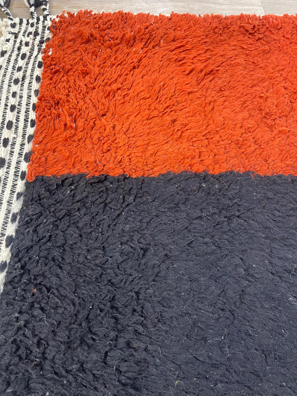 Gros plan sur la laine du tapis berbère Guelmim, poil orange et noir noué à la main