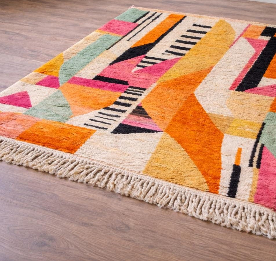 Tapis berbère graphique orange et rose Tinfou posé au sol vu de trois quarts, noué main au Maroc