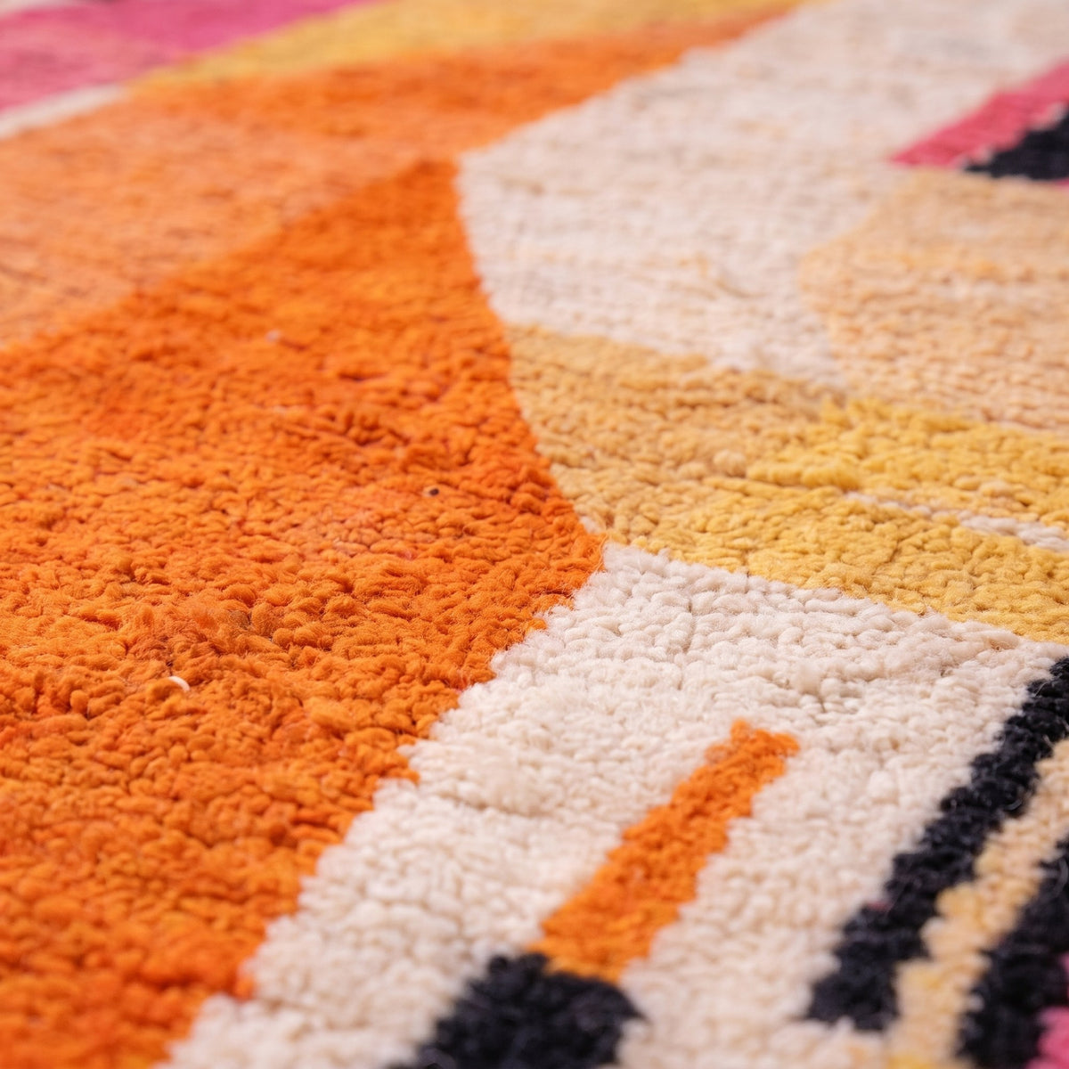 Gros plan sur un motif du tapis berbère Tinfou, fond écru en aplats géométriques orange