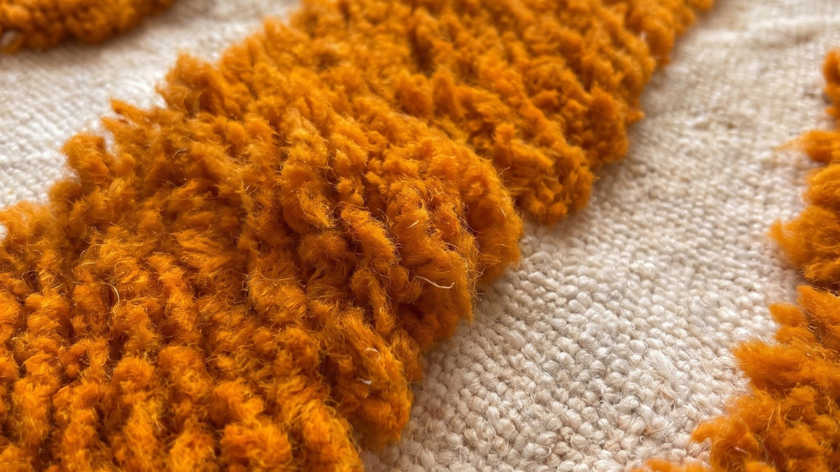 Gros plan sur la laine du tapis berbère Tazemurt, poil orange noué à la main