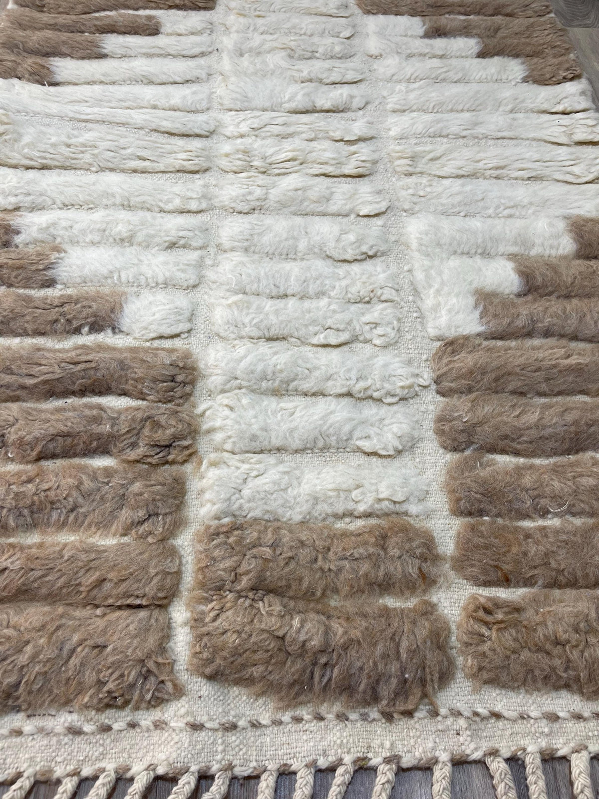 Gros plan sur un détail du tapis berbère Tarkeddit, poil long et motif taupe et blanc vus de près