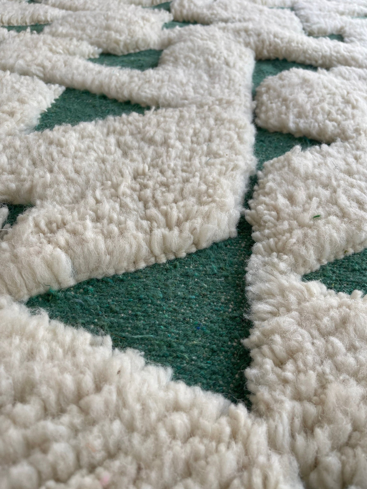 Gros plan sur la laine du tapis berbère Sezlan, laine de mouton au poil long, verte et blanche