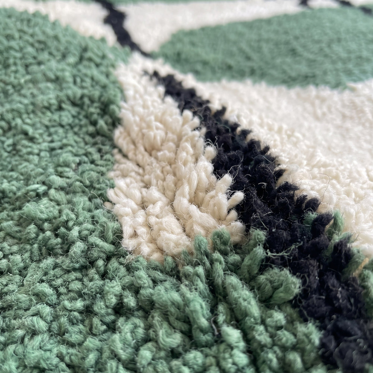 Gros plan sur un motif du tapis berbère Azrou, fond vert forêt à poil long