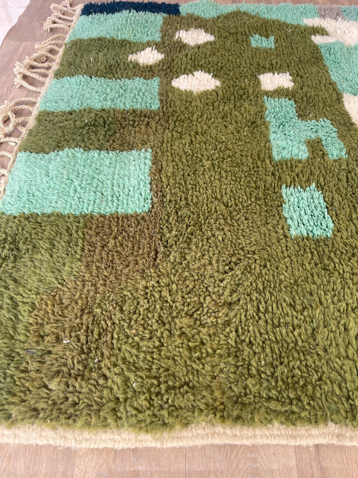 Gros plan sur un détail du tapis berbère Issafen, poil long et motif vert olive vus de près