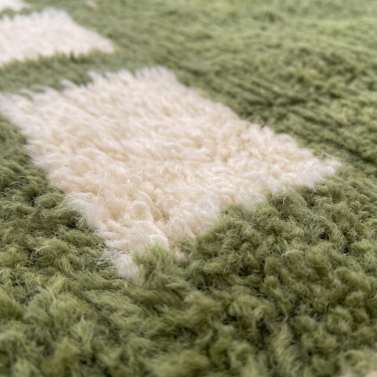 Gros plan sur un motif du tapis berbère Tazouta, fond vert mousse encadré de vingt-quatre carrés ivoire