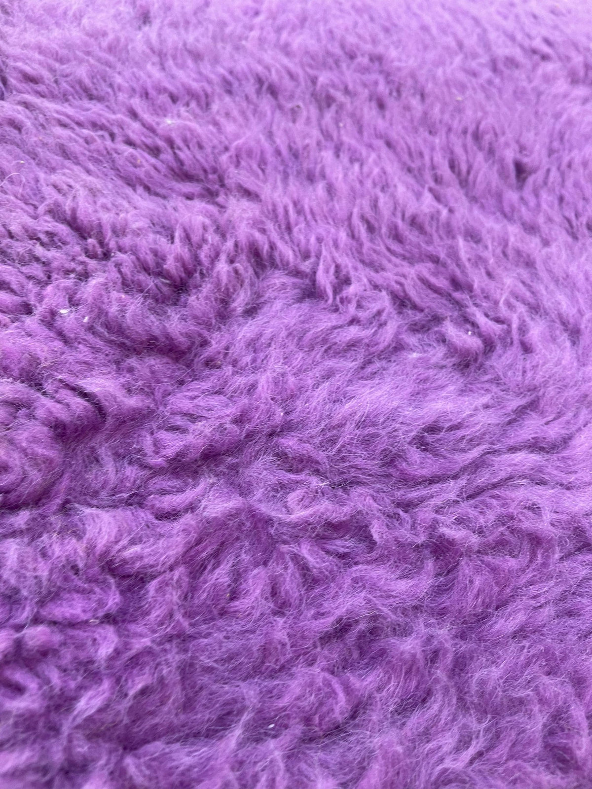 Gros plan sur la laine du tapis berbère Tamghra, laine de mouton au poil long, violette et jaune
