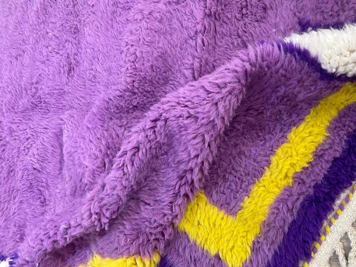 Gros plan sur un détail du tapis berbère Tamghra, poil long et motif violet et jaune vus de près