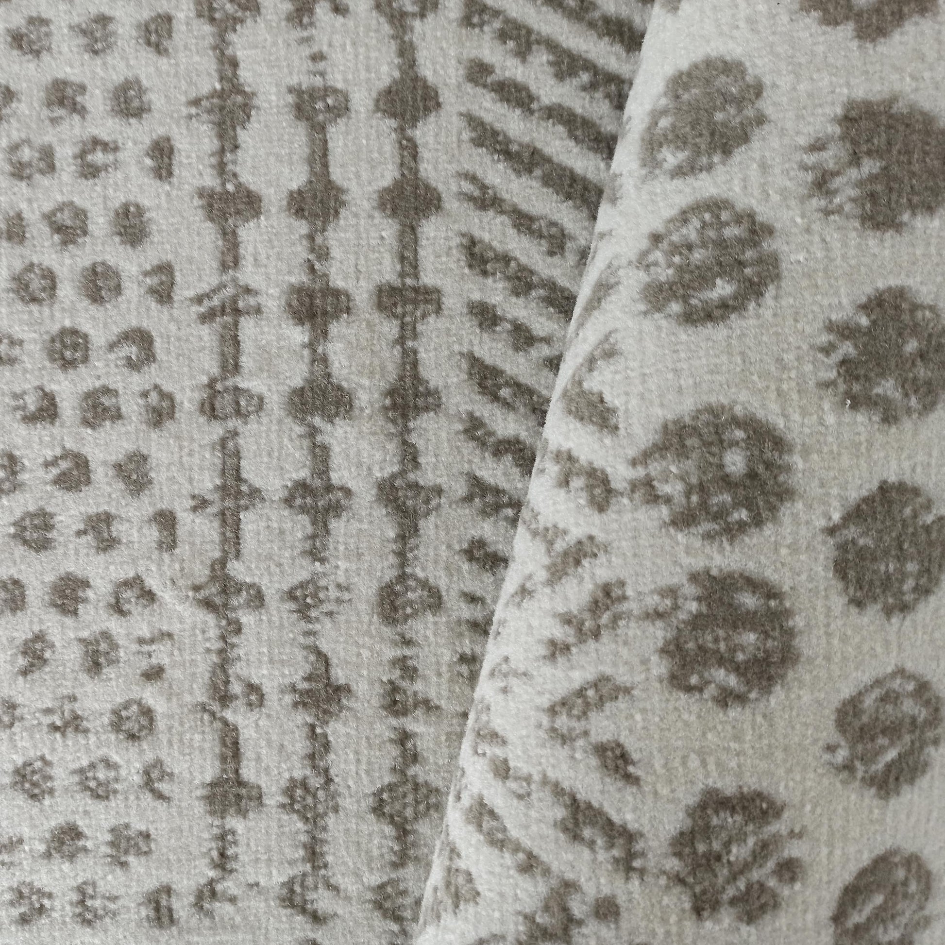 Tapis moelleux beige et gris avec des motifs allant de formes géométriques à de grandes taches, visiblement plié