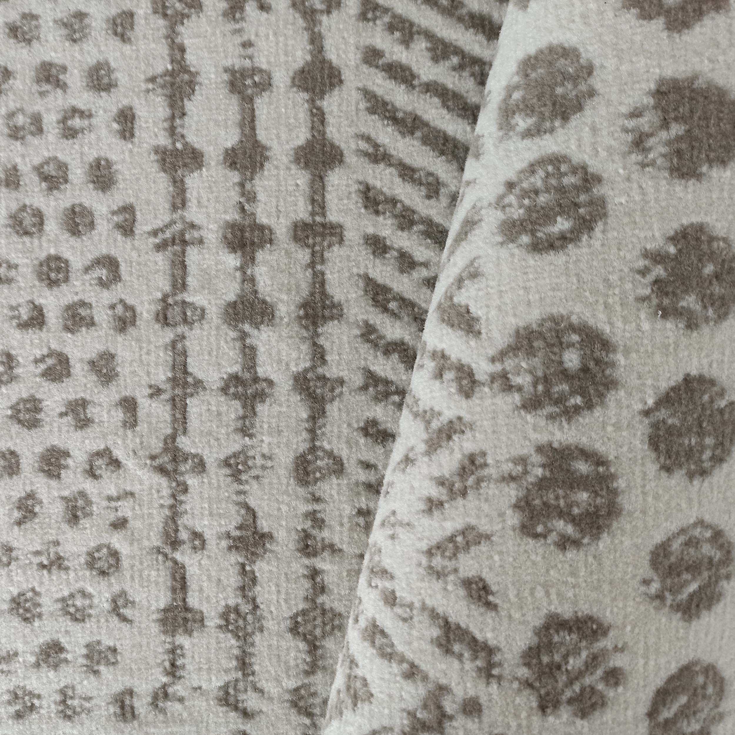 Tapis moelleux beige et gris avec des motifs allant de formes géométriques à de grandes taches, visiblement plié