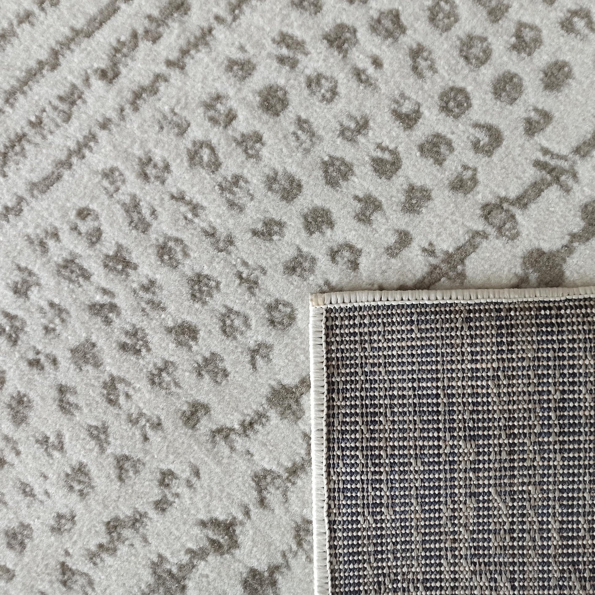 Tapis à motifs abstraits gris clair et foncé, dont un coin est retourné révélant son envers tissé