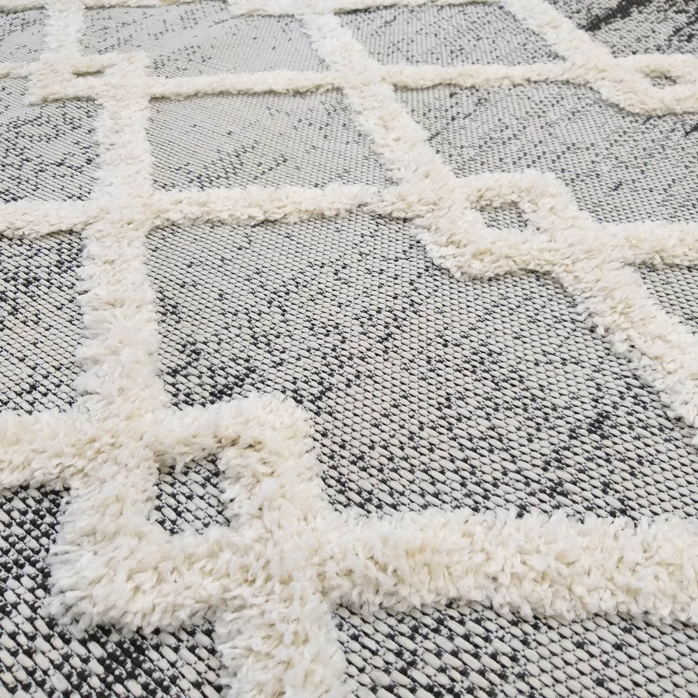 Tapis à motif géométrique blanc cassé, shaggy et en relief, sur un fond tissé moucheté gris et noir