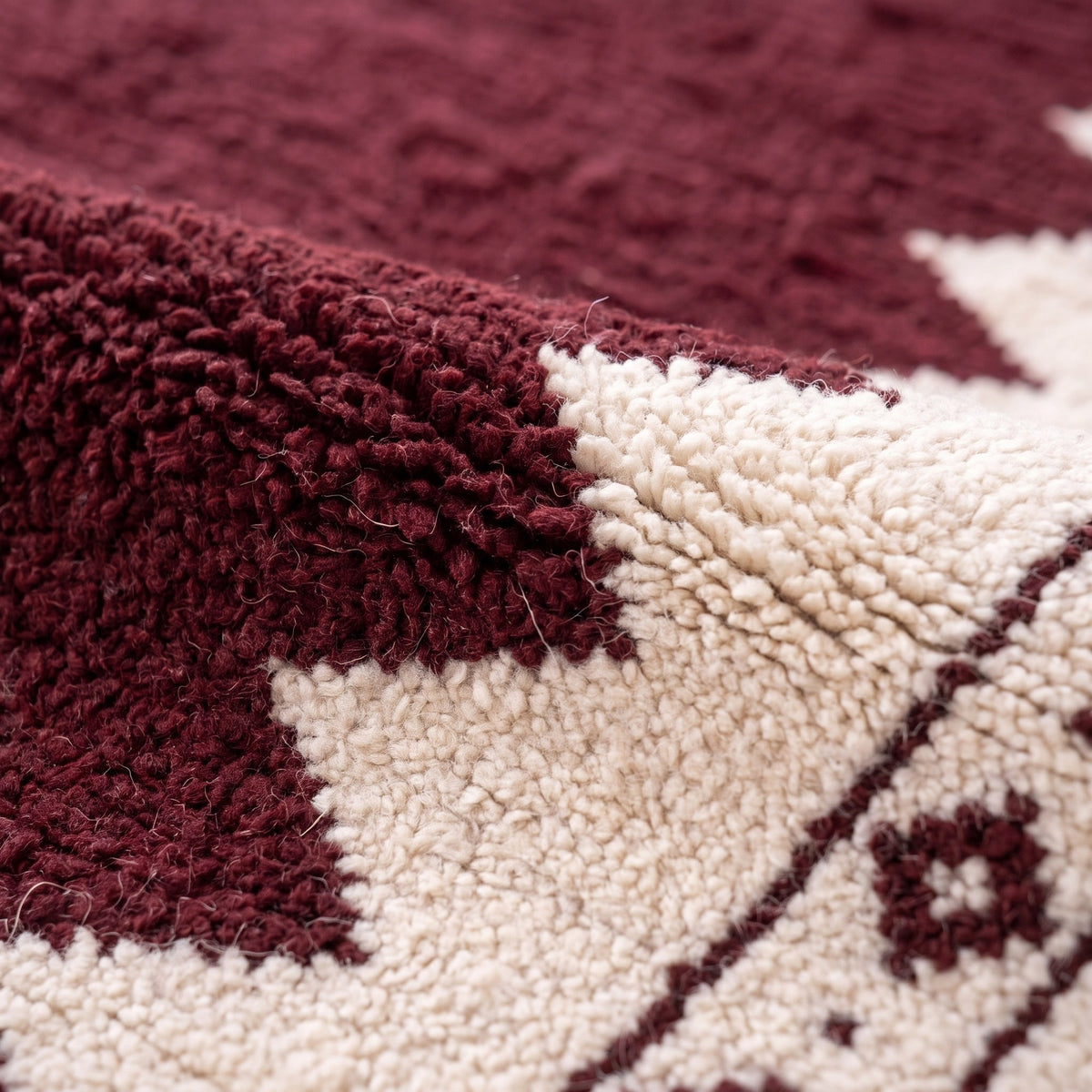 Gros plan sur un motif du tapis berbère Tasgalt, champ bordeaux aux longs côtés dentelés en dents