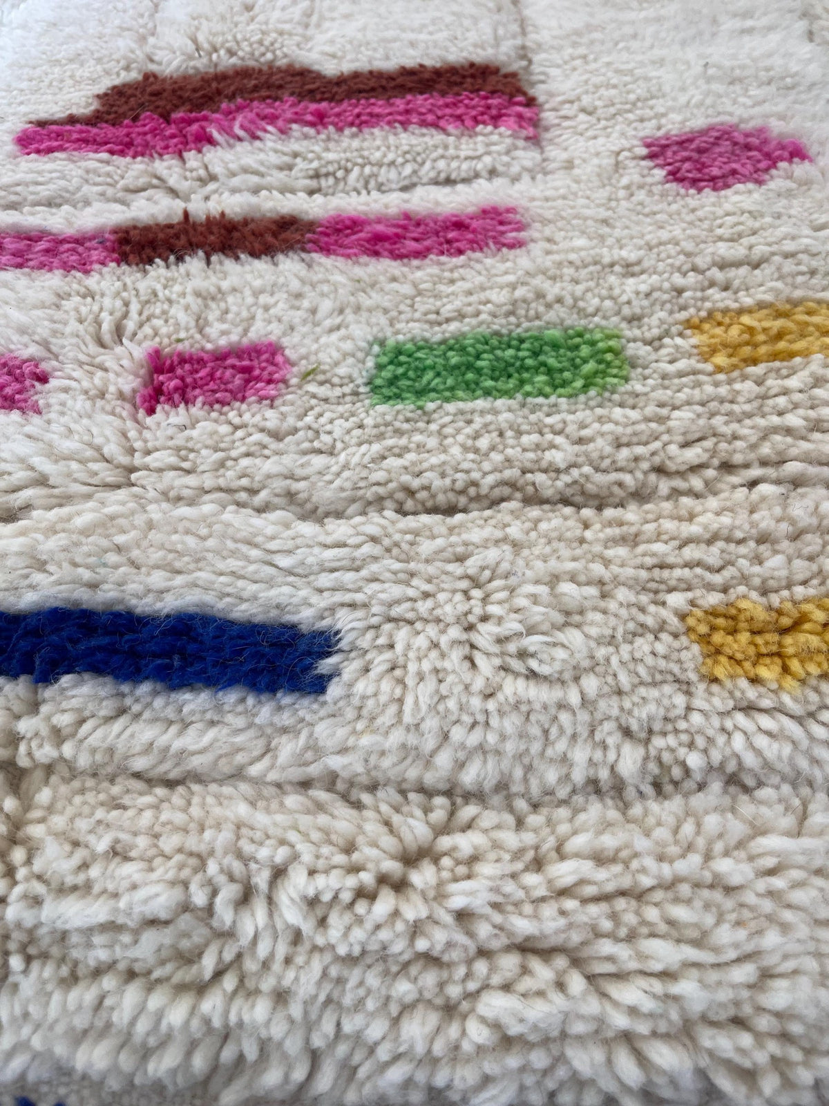 Gros plan sur la laine du tapis berbère Kermila, laine de mouton au poil long, blanche et rose