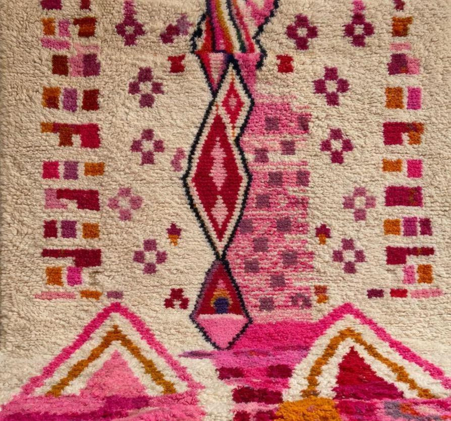 Gros plan sur un détail du tapis berbère Tirzana, poil long et motif blanc et rose vus de près