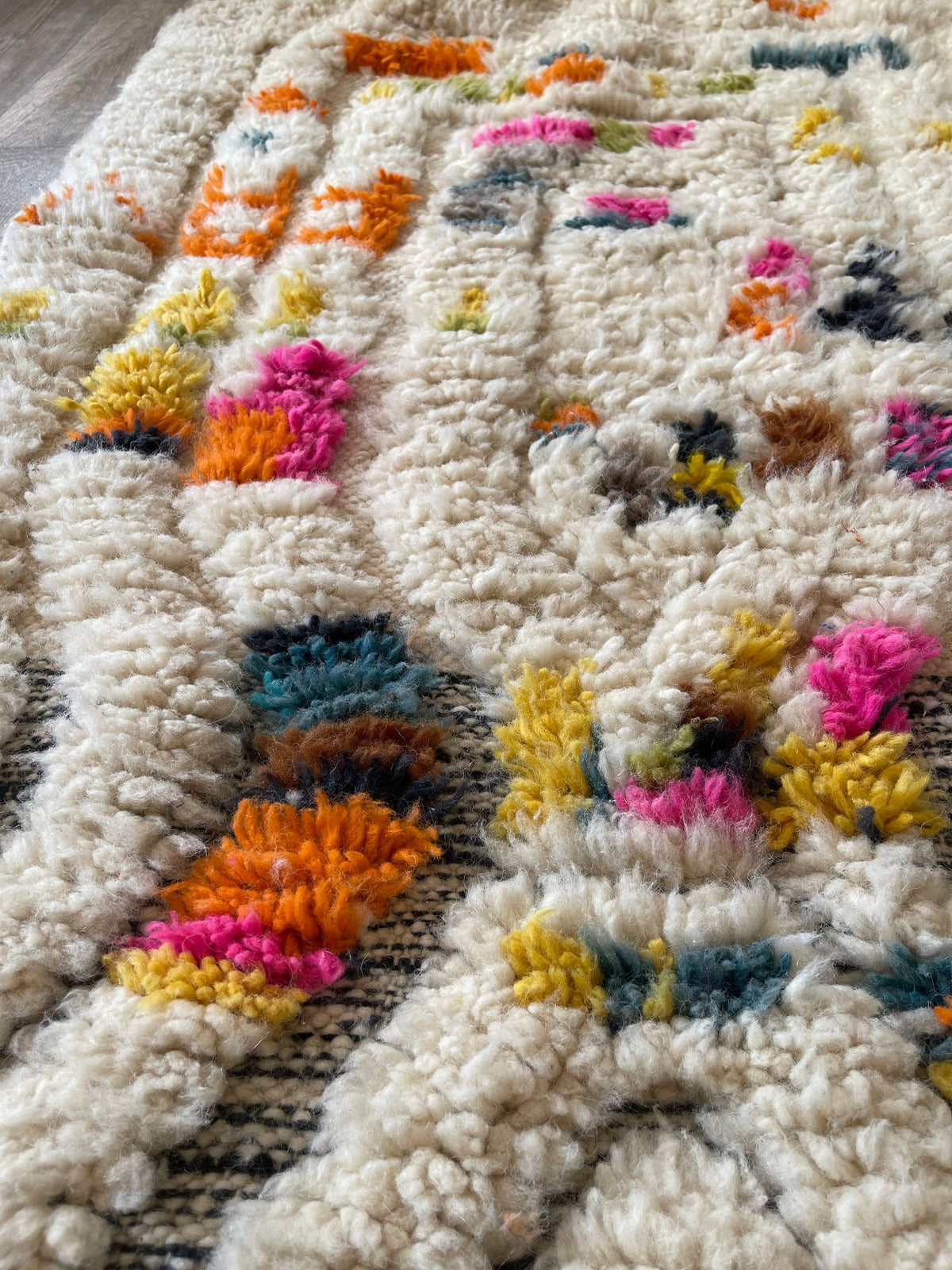 Gros plan sur un détail du tapis berbère Asni, poil long et motif blanc multicolore vus de près