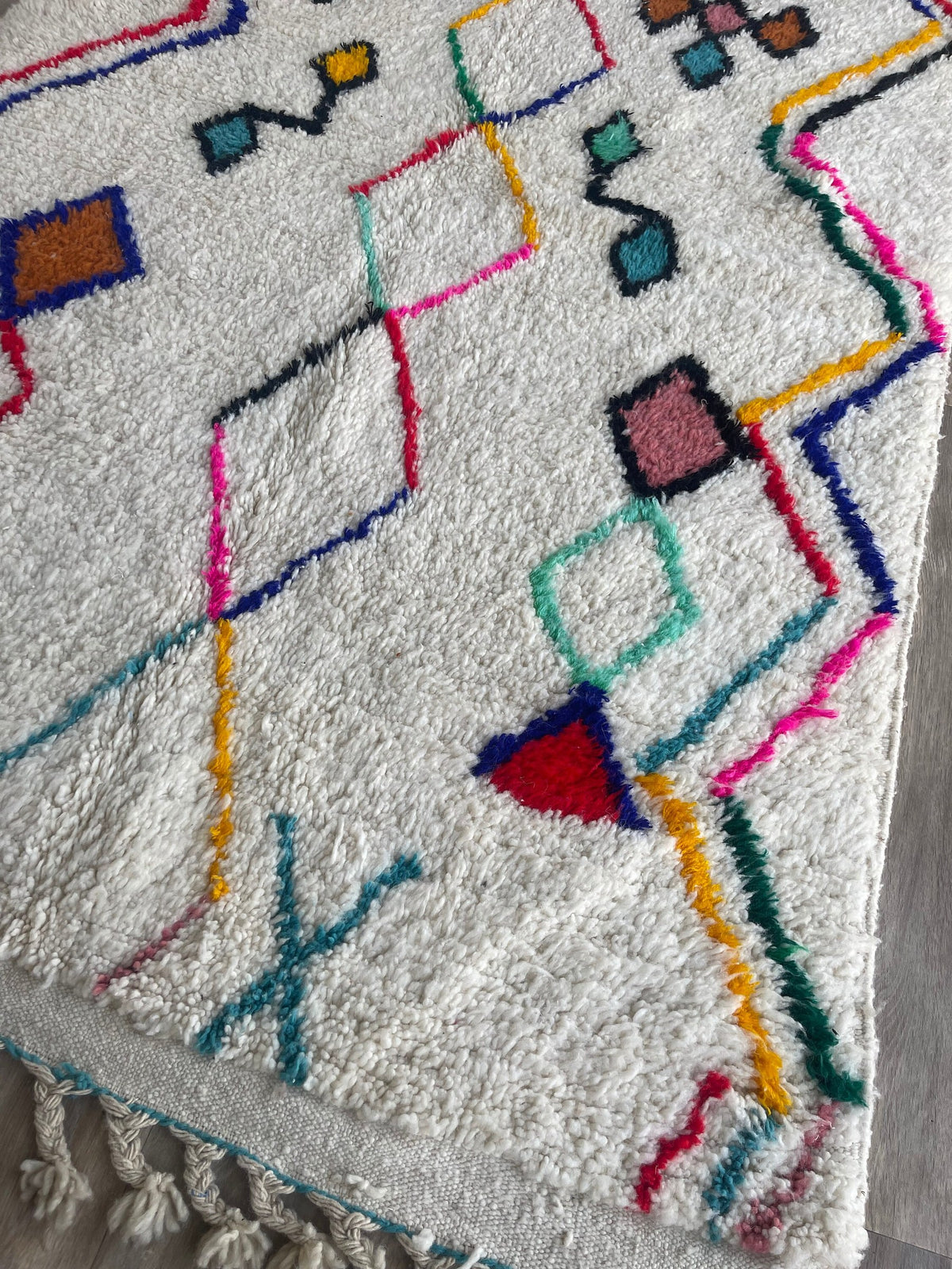 Gros plan sur le coin relevé du tapis berbère Tafirwa, épaisseur du poil long et dos tissé à la main