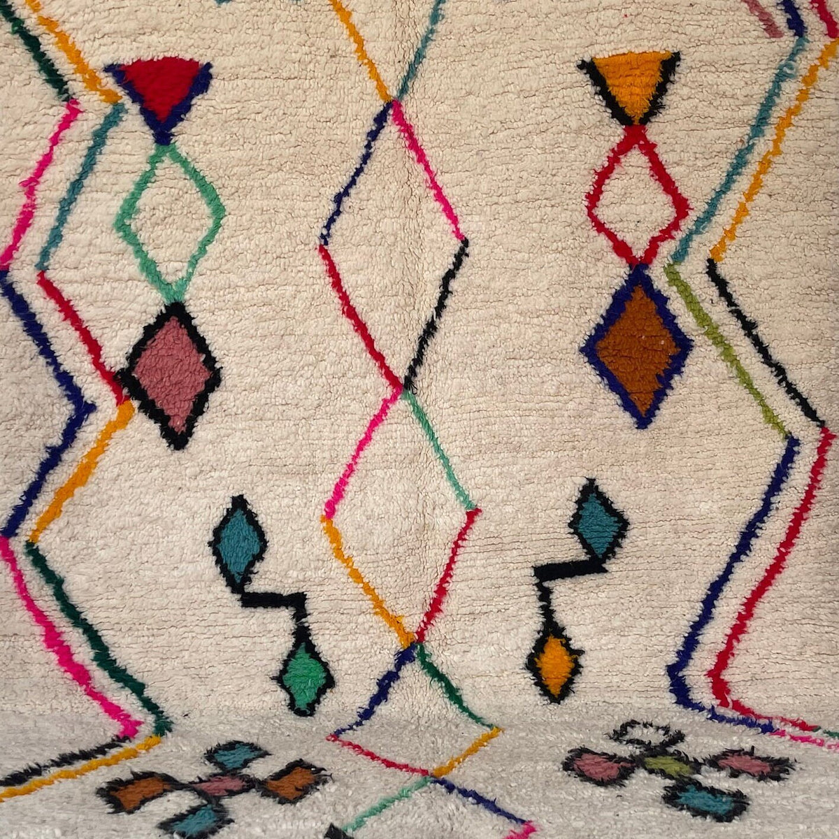 Gros plan sur un détail du tapis berbère Tafirwa, poil long et motif blanc multicolore vus de près