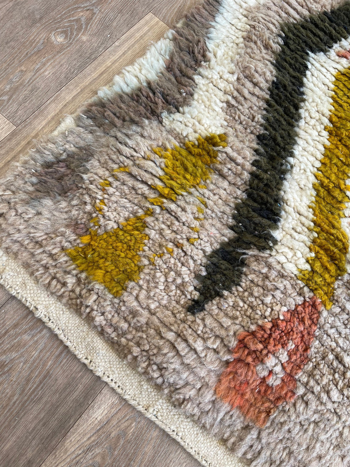 Gros plan sur le coin relevé du tapis berbère Nabroud, épaisseur du poil long et dos tissé à la main