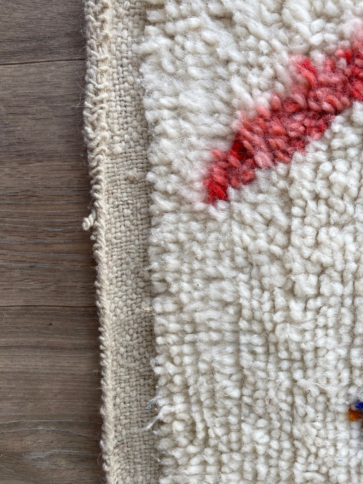 Gros plan sur le coin relevé du tapis berbère Demnate, épaisseur du poil long et dos tissé à la main
