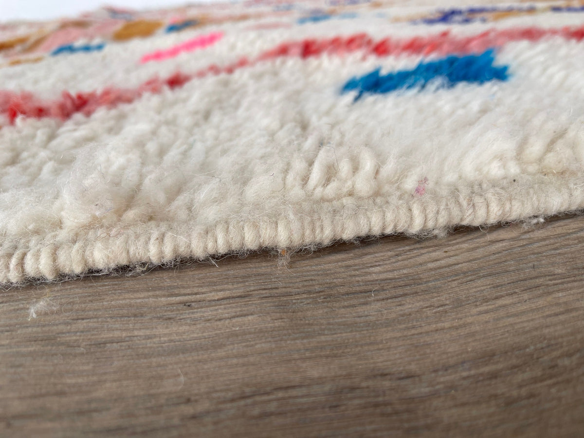 Gros plan sur le coin relevé du tapis berbère Demnate, bordure et envers visibles de près