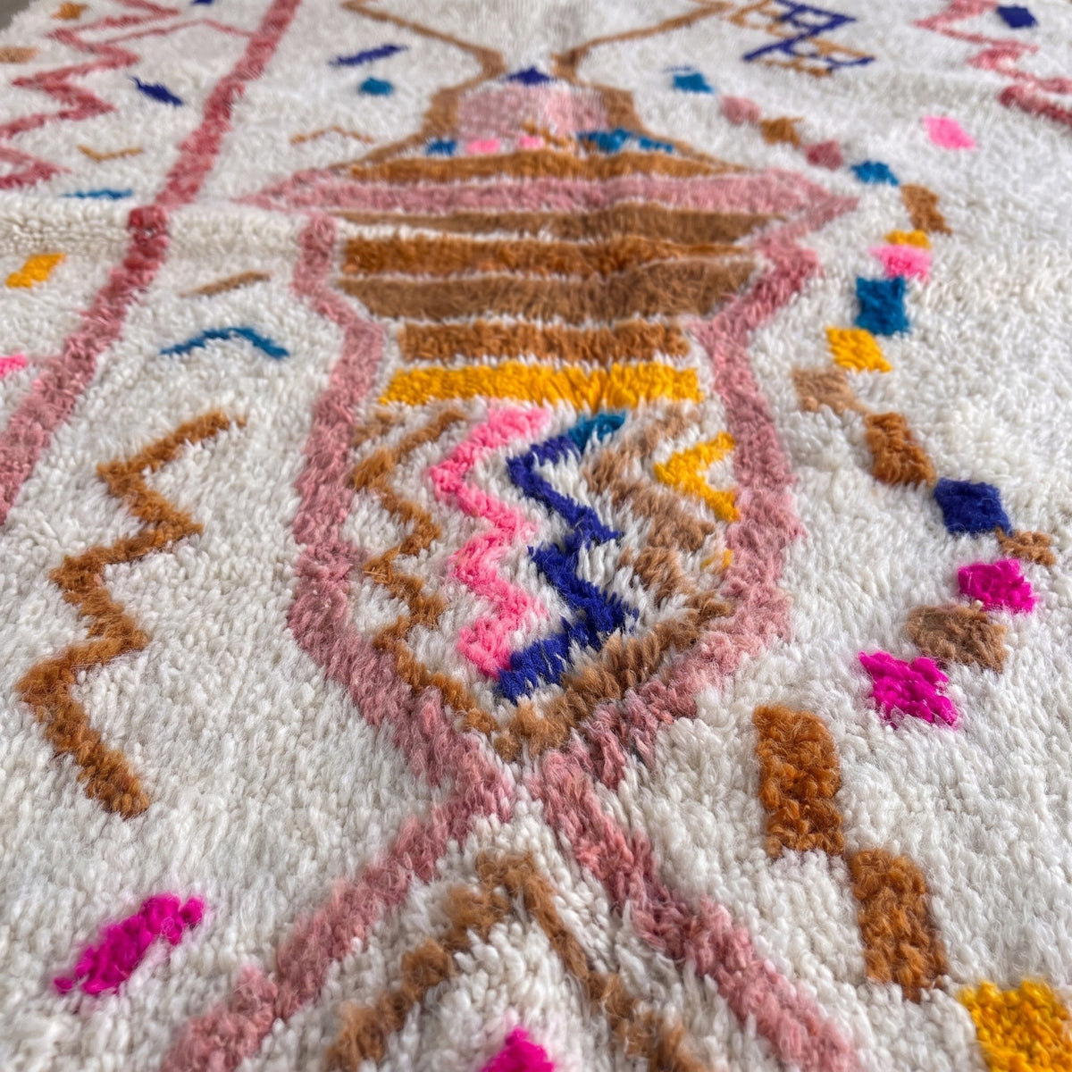 Gros plan sur un motif du tapis berbère Demnate, fond ivoire à poil long, sablier brun