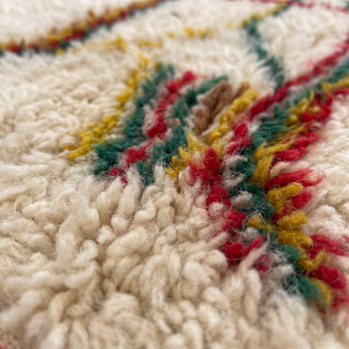 Gros plan sur un motif du tapis berbère Tabant, fond ivoire à poil long, à gauche