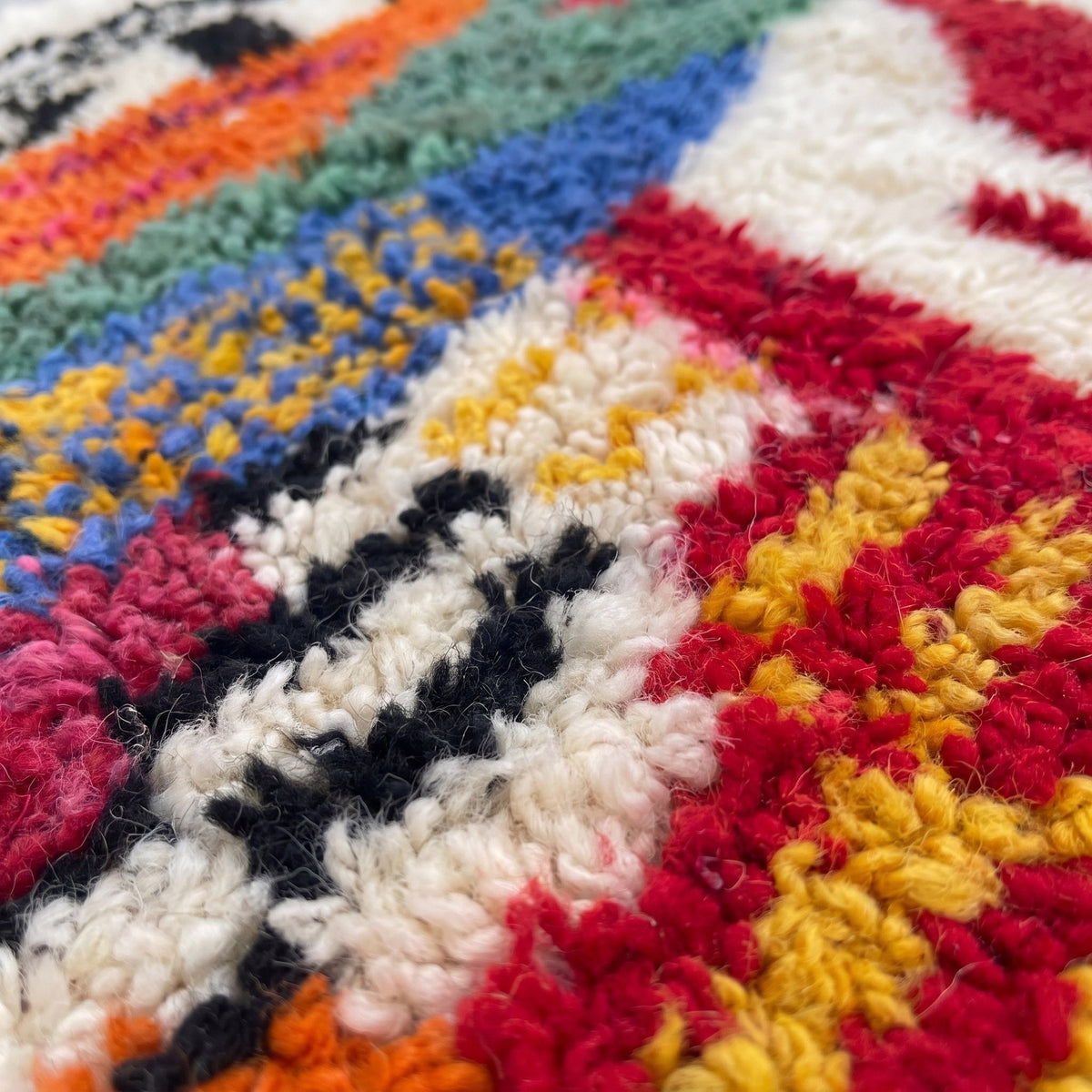 Gros plan sur un motif du tapis berbère Tamawayt, fond ivoire à poil long, grande figure multicolore