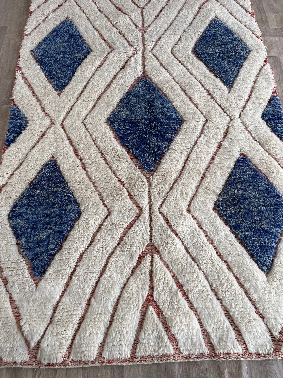 Gros plan sur un détail du tapis berbère Aman, poil long et motif blanc et bleu vus de près