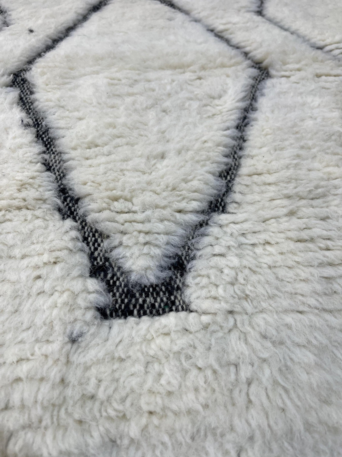 Gros plan sur la laine du tapis berbère Elzira, laine de mouton au poil long, blanche et noire