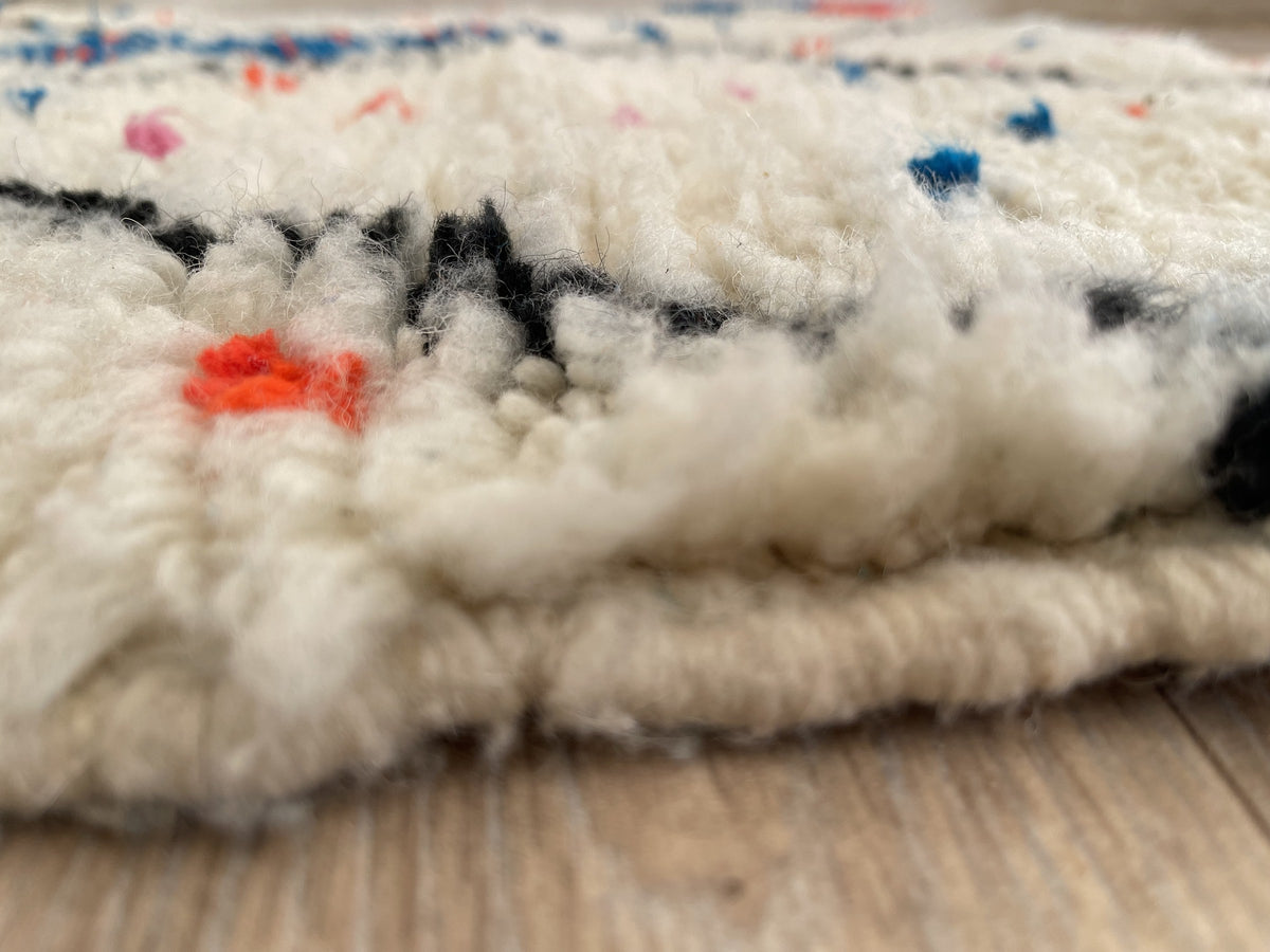Gros plan sur le coin relevé du tapis berbère Idmim, épaisseur du poil long et dos tissé à la main