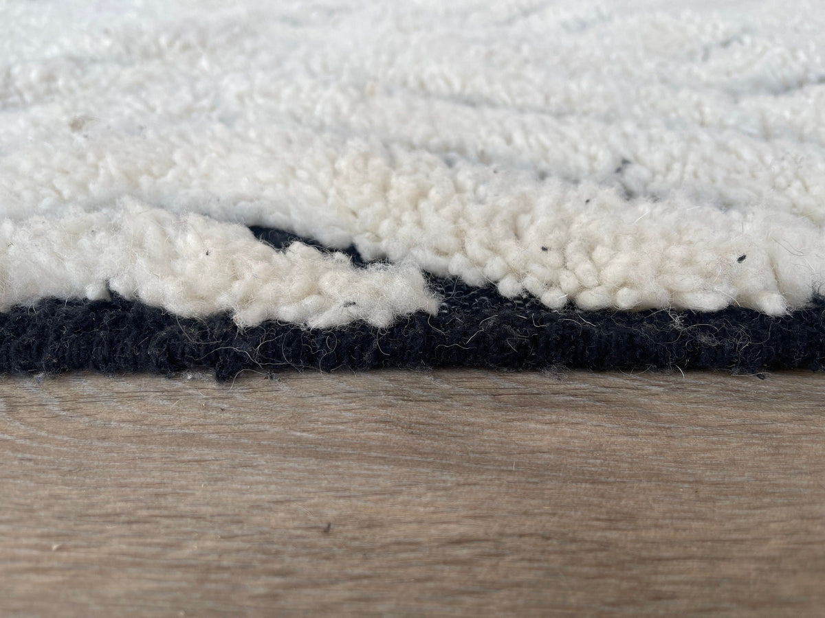 Gros plan sur le coin relevé du tapis berbère Ousmil, épaisseur du poil long et dos tissé à la main
