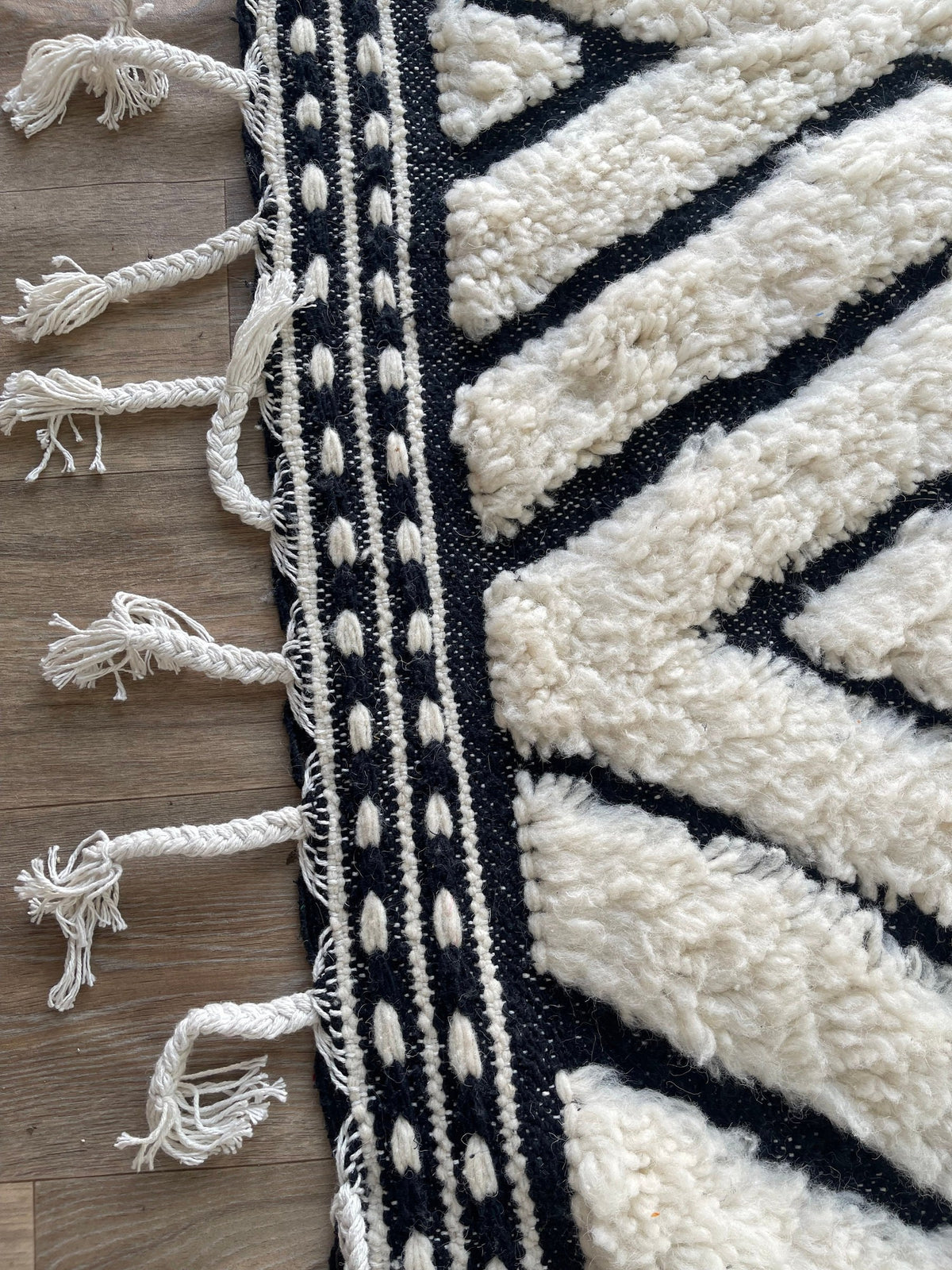 Gros plan sur les franges du tapis berbère Ousmil, blanches tressées en bas, nouées à la main