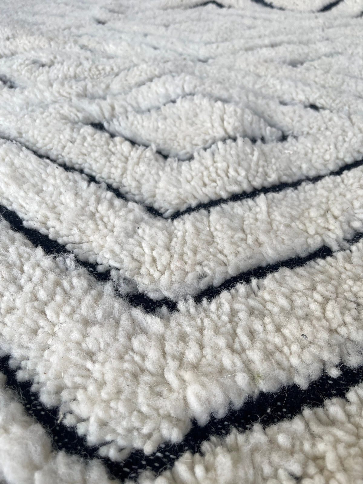 Gros plan sur la laine du tapis berbère Ousmil, laine de mouton au poil long, blanche et noire