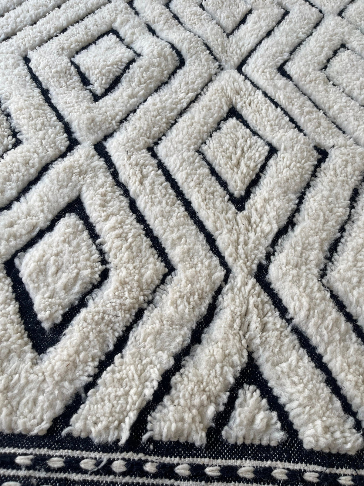 Gros plan sur la laine du tapis berbère Ousmil, relief de la laine et du motif à la lumière