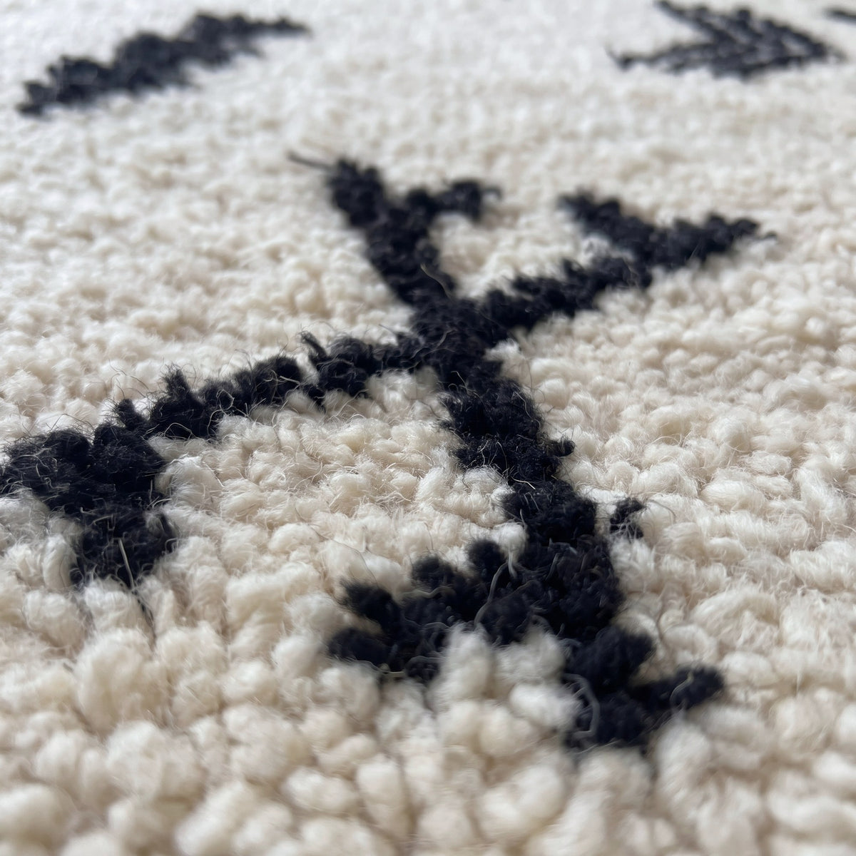 Gros plan sur un motif du tapis berbère Tasusmi, fond ivoire à poil long, une trentaine