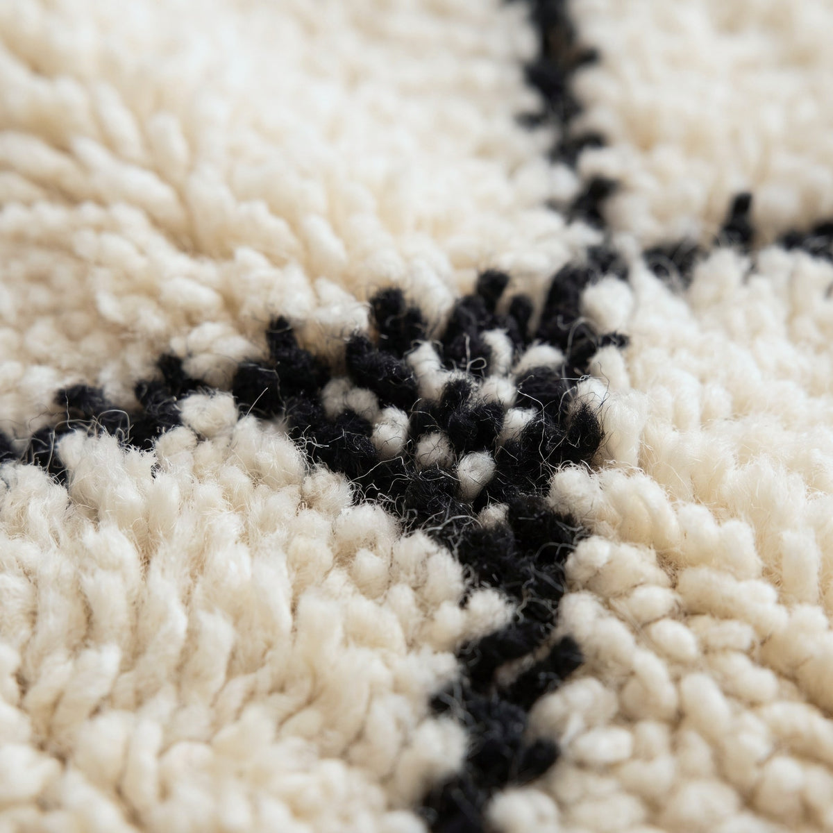 Gros plan sur un motif du tapis berbère Tiziri, fond écru très clair à poil long