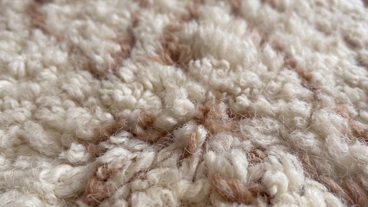 Gros plan sur la laine du tapis berbère Timoulay, poil blanc et rose noué à la main
