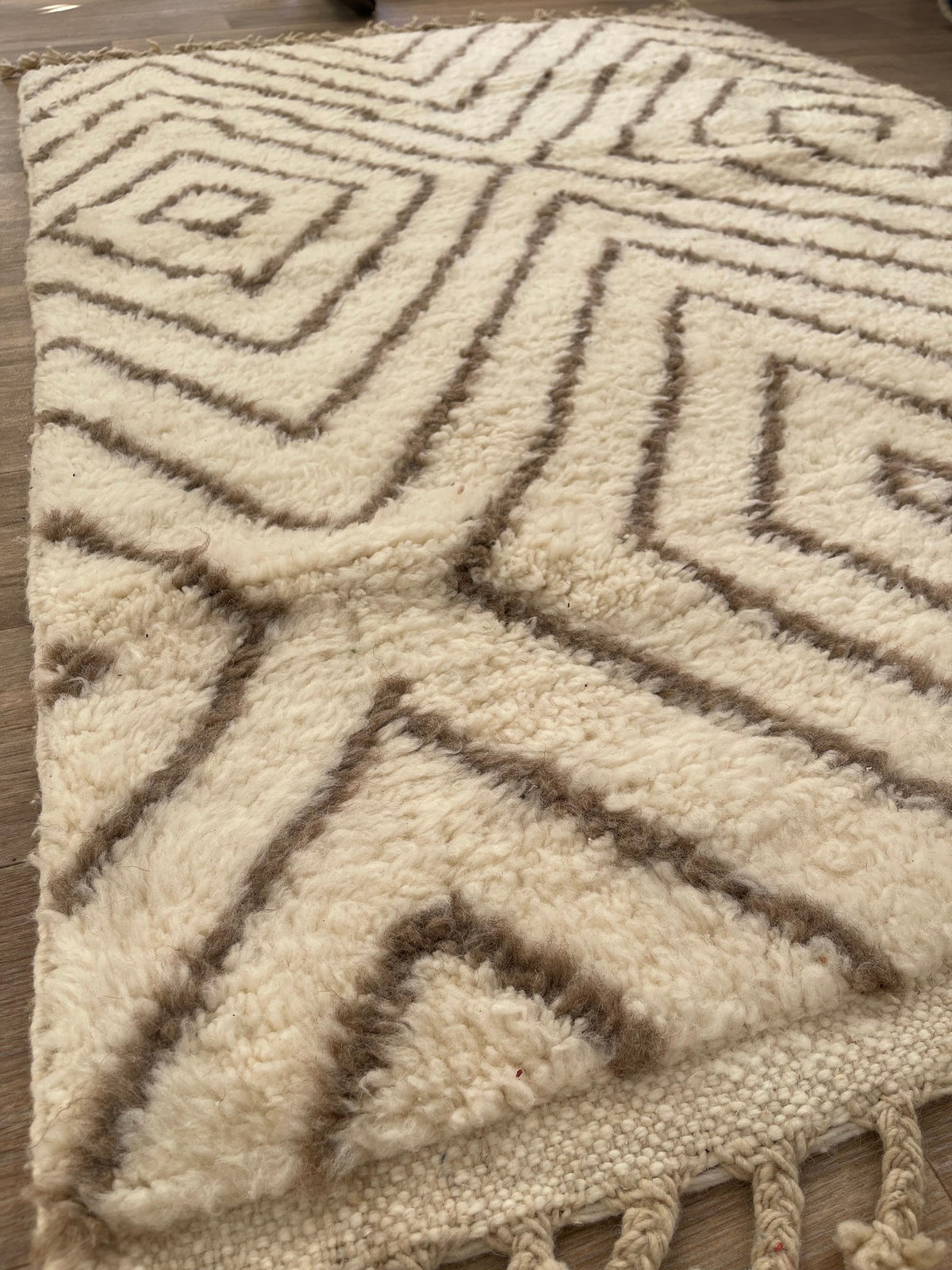 Gros plan sur un détail du tapis berbère Almis, poil long et motif blanc et taupe vus de près