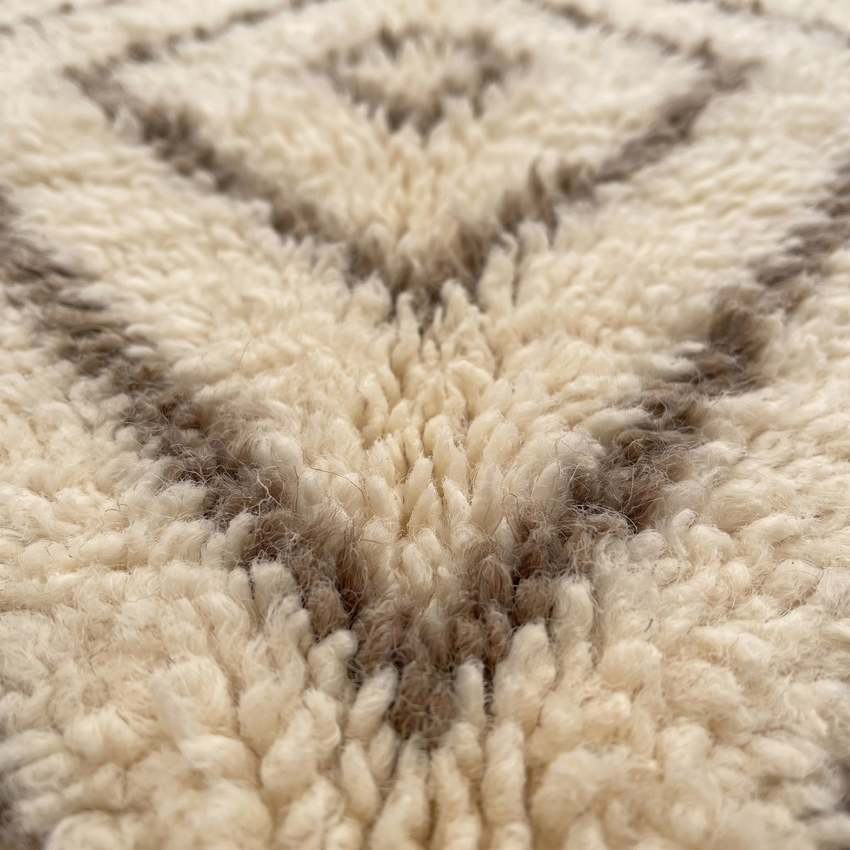 Gros plan sur un motif du tapis berbère Almis, fond ivoire, fines lignes brun taupe