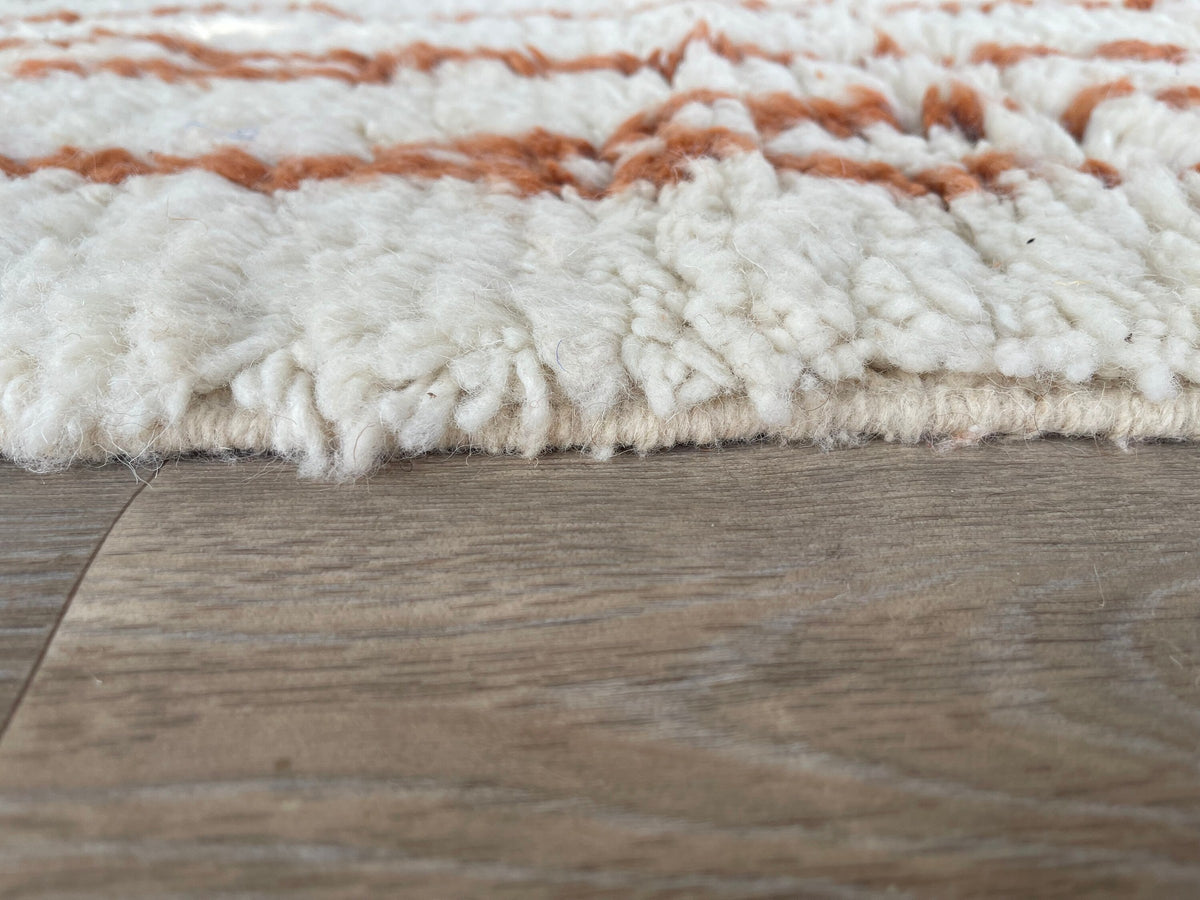 Gros plan sur le coin relevé du tapis berbère Aghanim, épaisseur du poil long et dos tissé à la main