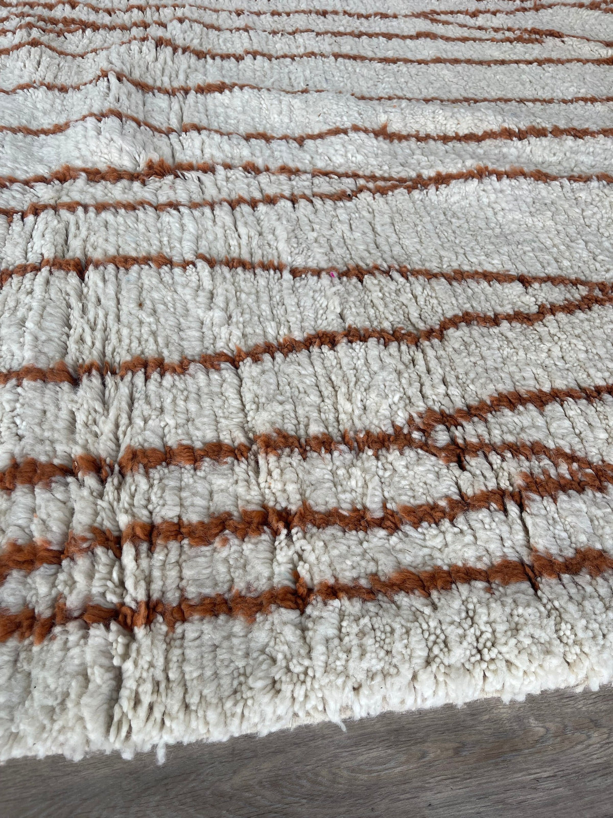 Gros plan sur un détail du tapis berbère Aghanim, poil long et motif blanc et terracotta vus de près