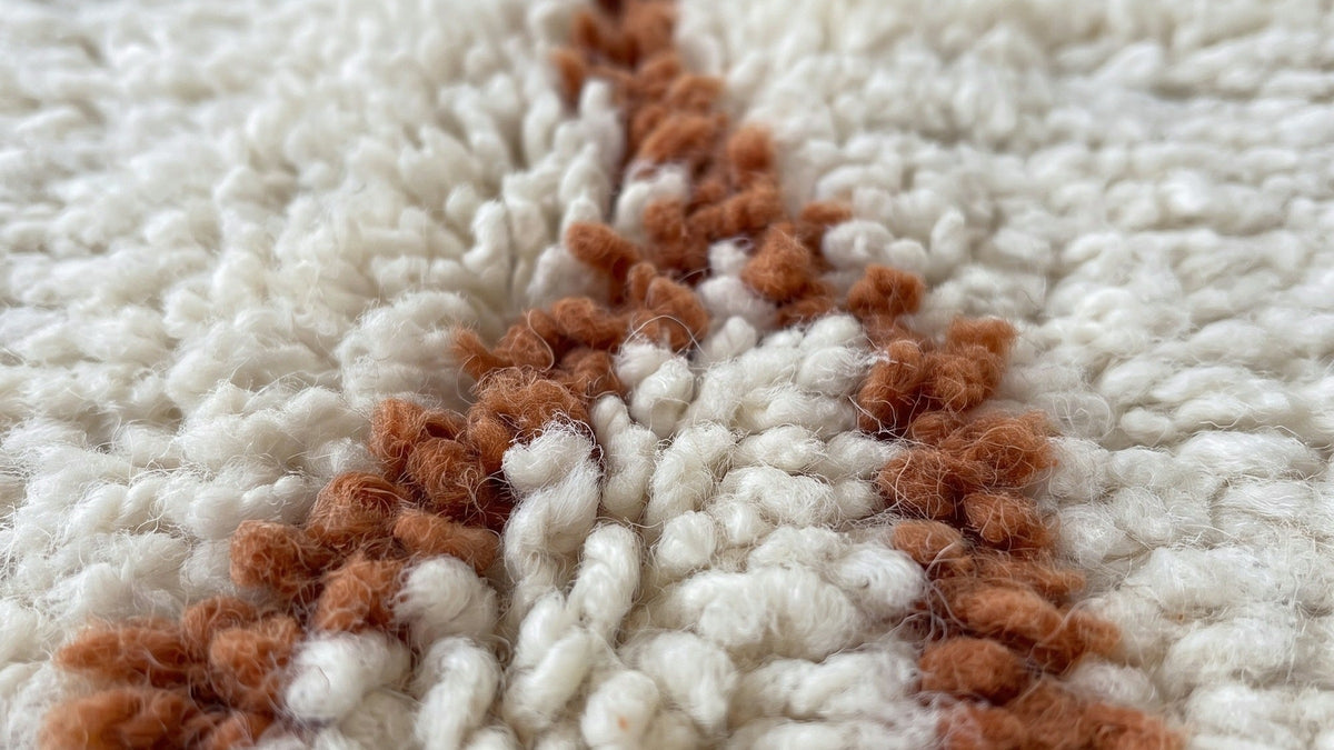 Gros plan sur la laine du tapis berbère Aghanim, poil blanc et terracotta noué à la main